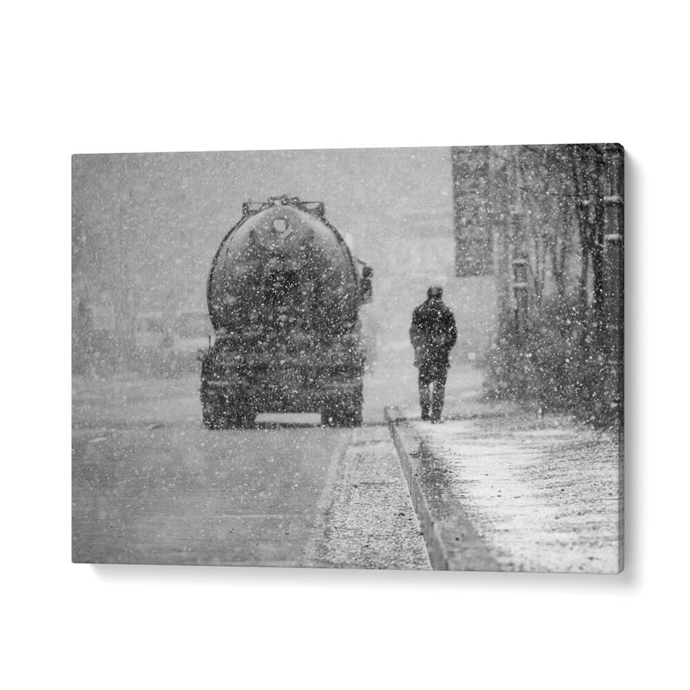 A solitary figure walks in a snowstorm near a large vehicle, showcasing HEAVY THINGS, PHOTOGRAPHY PRINTS elegance.
