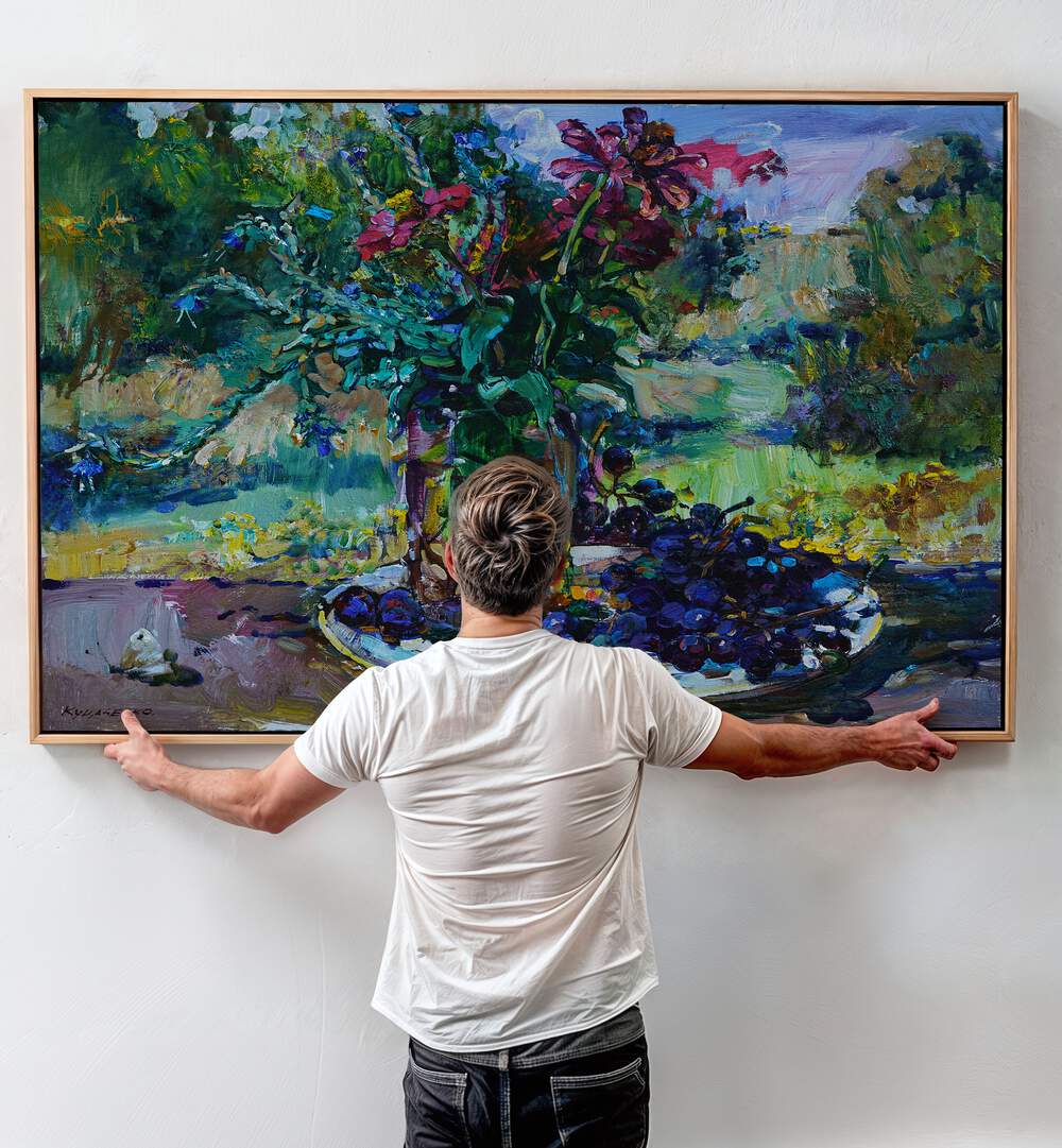 A person admires the vibrant WILDFLOWERS AND GRAPES, FLORAL FLOWER PAINTINGS, enhancing their home decor beautifully.