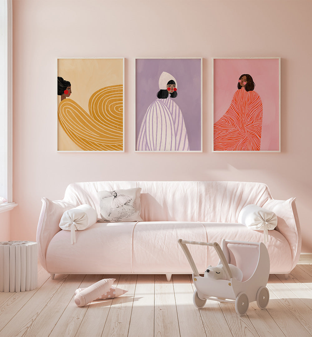 Three colorful abstract art pieces on a wall above a white sofa with a toy stroller in a room.