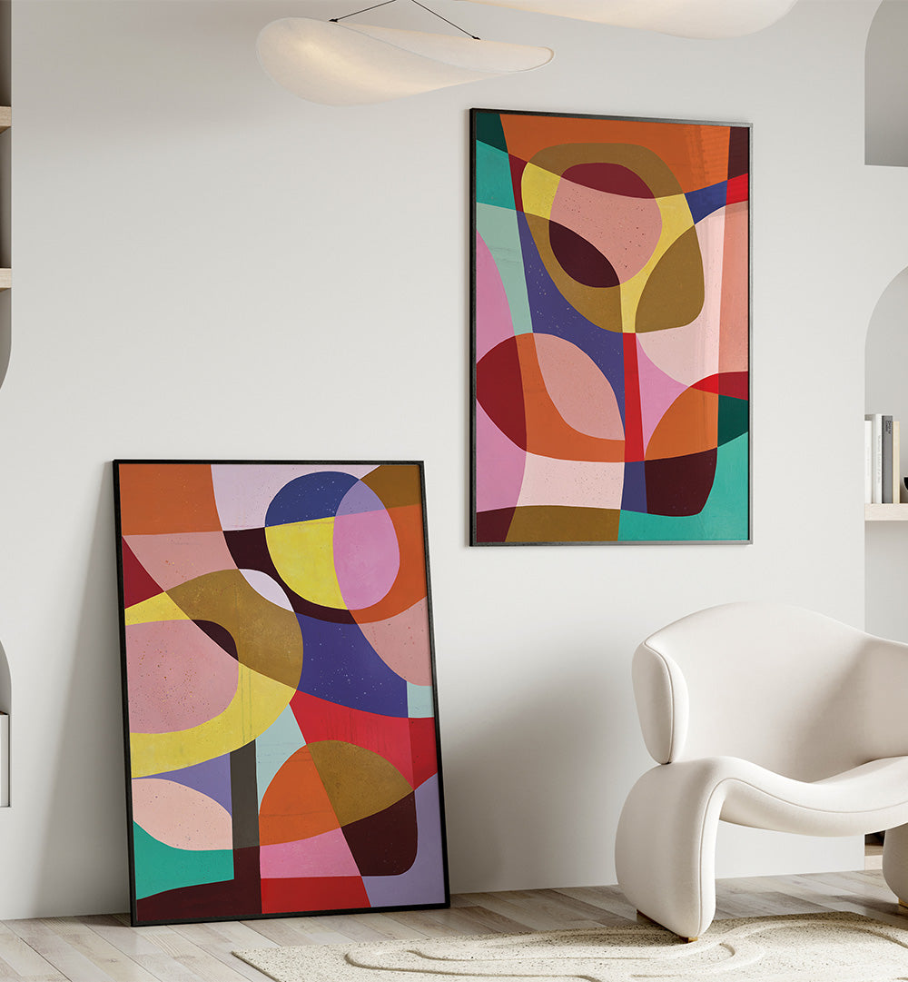 Two abstract art pieces in vibrant colors on a white wall with a modern chair.