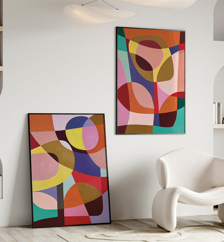 Two abstract art pieces in vibrant colors on a white wall with a modern chair.