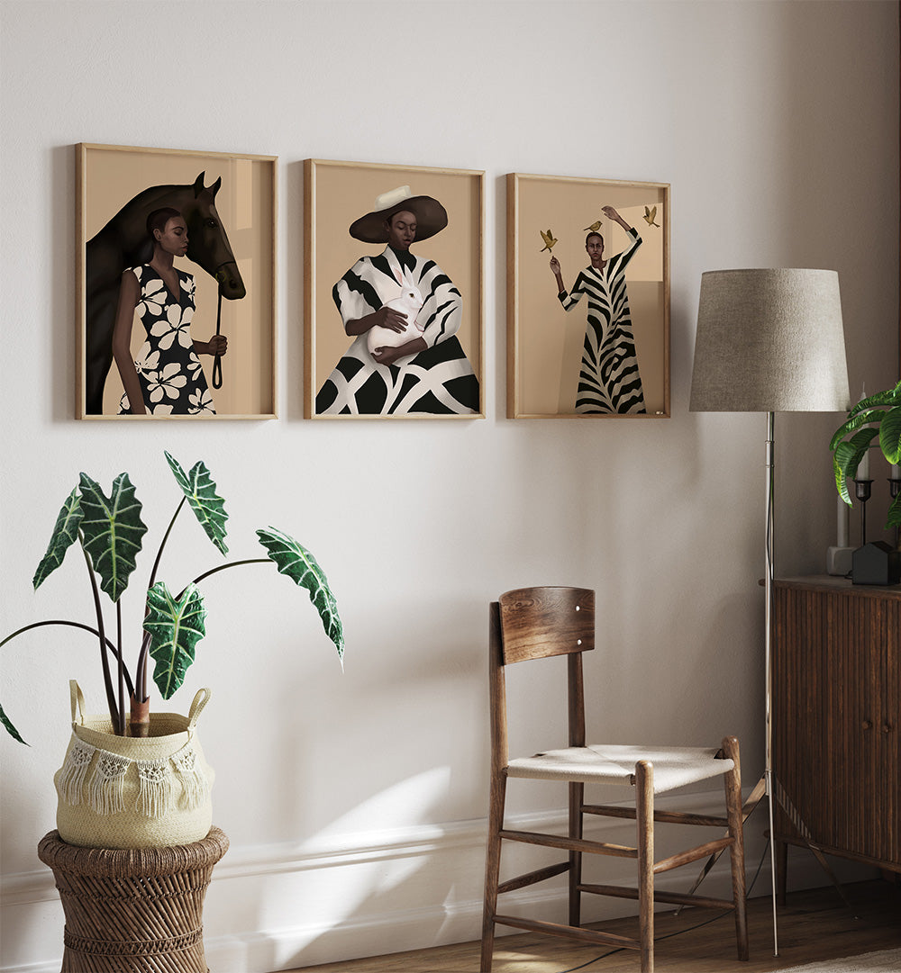 Three framed artworks on a wall with a chair, lamp, and plant in the foreground.