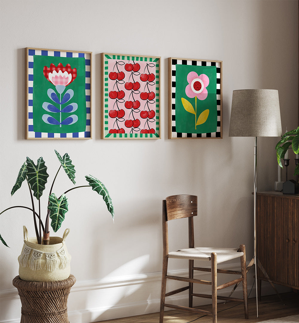 Three colorful floral and fruit-themed prints on a wall above a wooden chair.