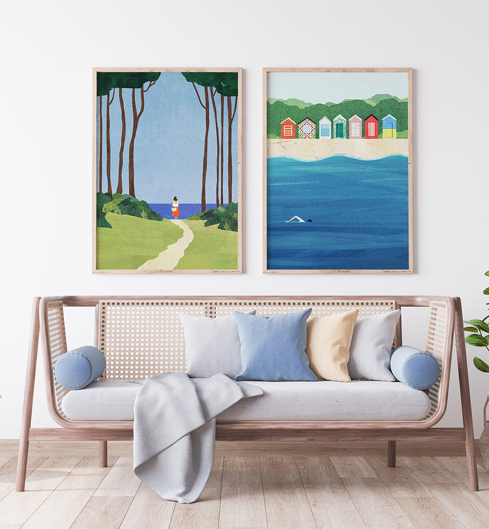Two framed artworks of a beach scene and a path with a person, displayed above a sofa with cushions.