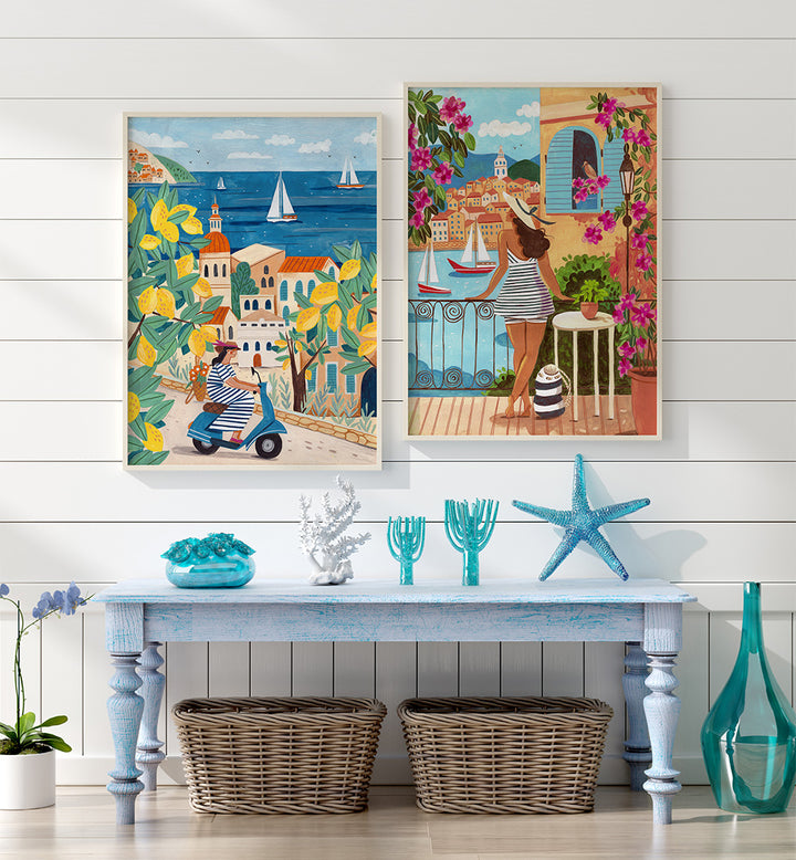 Two colorful paintings of Mediterranean scenes on a white wall above a table with decorative items.