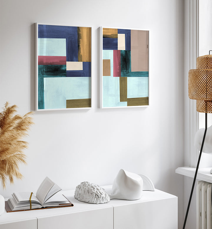 Two abstract art pieces on a white wall above a white console table with decorative items.