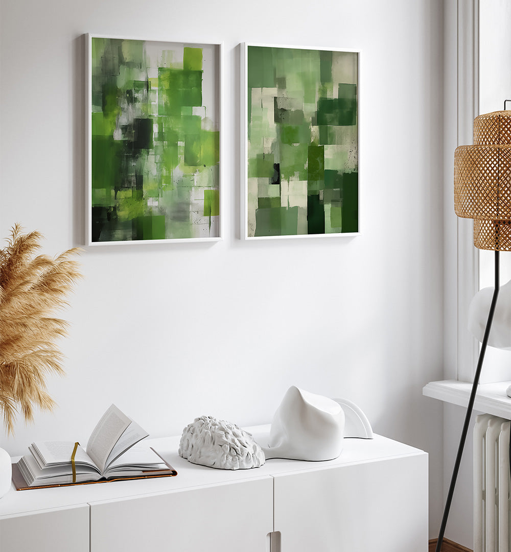 Two abstract green and gray paintings on a white wall above a white cabinet with decorative items.