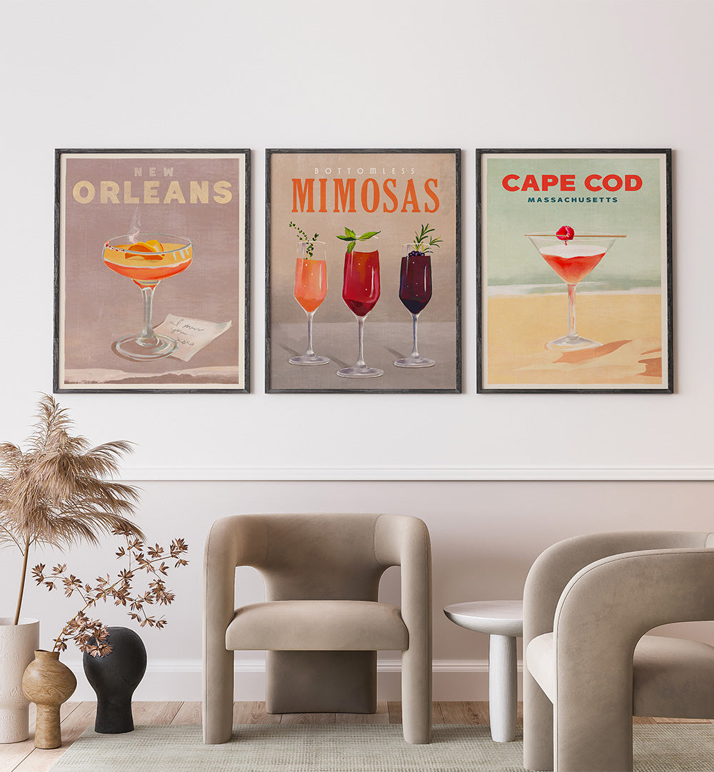 Three framed cocktail posters on a wall above modern chairs.