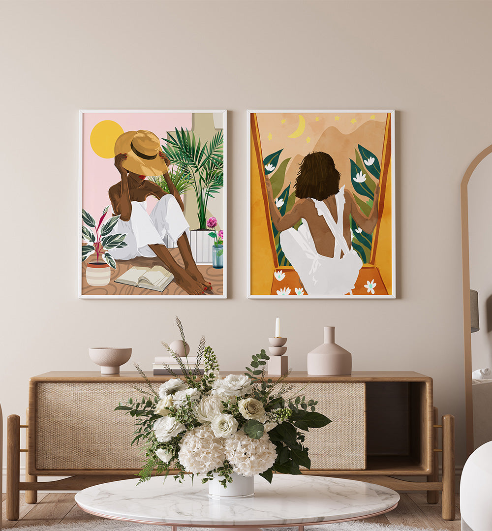 Two framed artworks of a woman sitting outdoors on a wall above a wooden console table with decorative items.