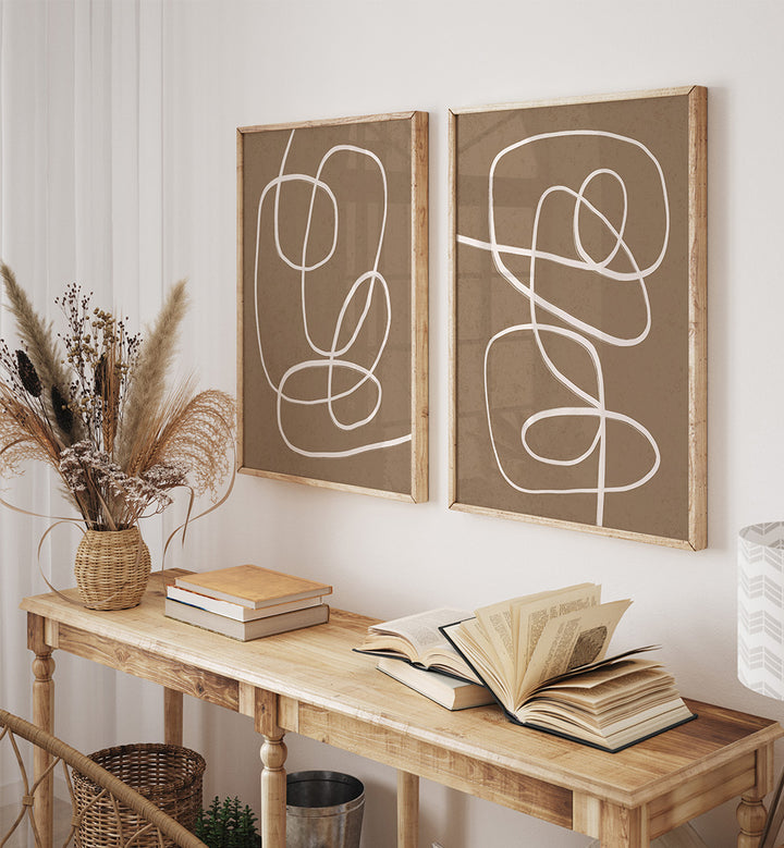 Two abstract line art paintings on a wall above a wooden console table with books and a vase.
