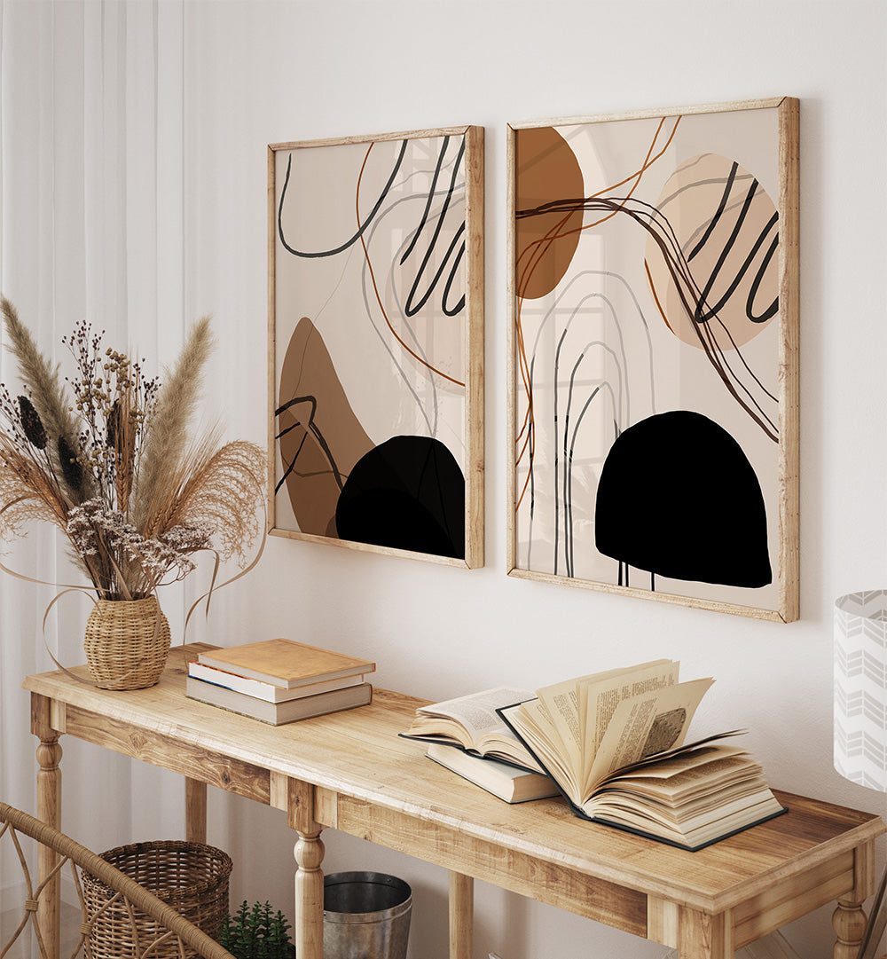 Two abstract art pieces on a wall above a wooden console table with books and a vase.