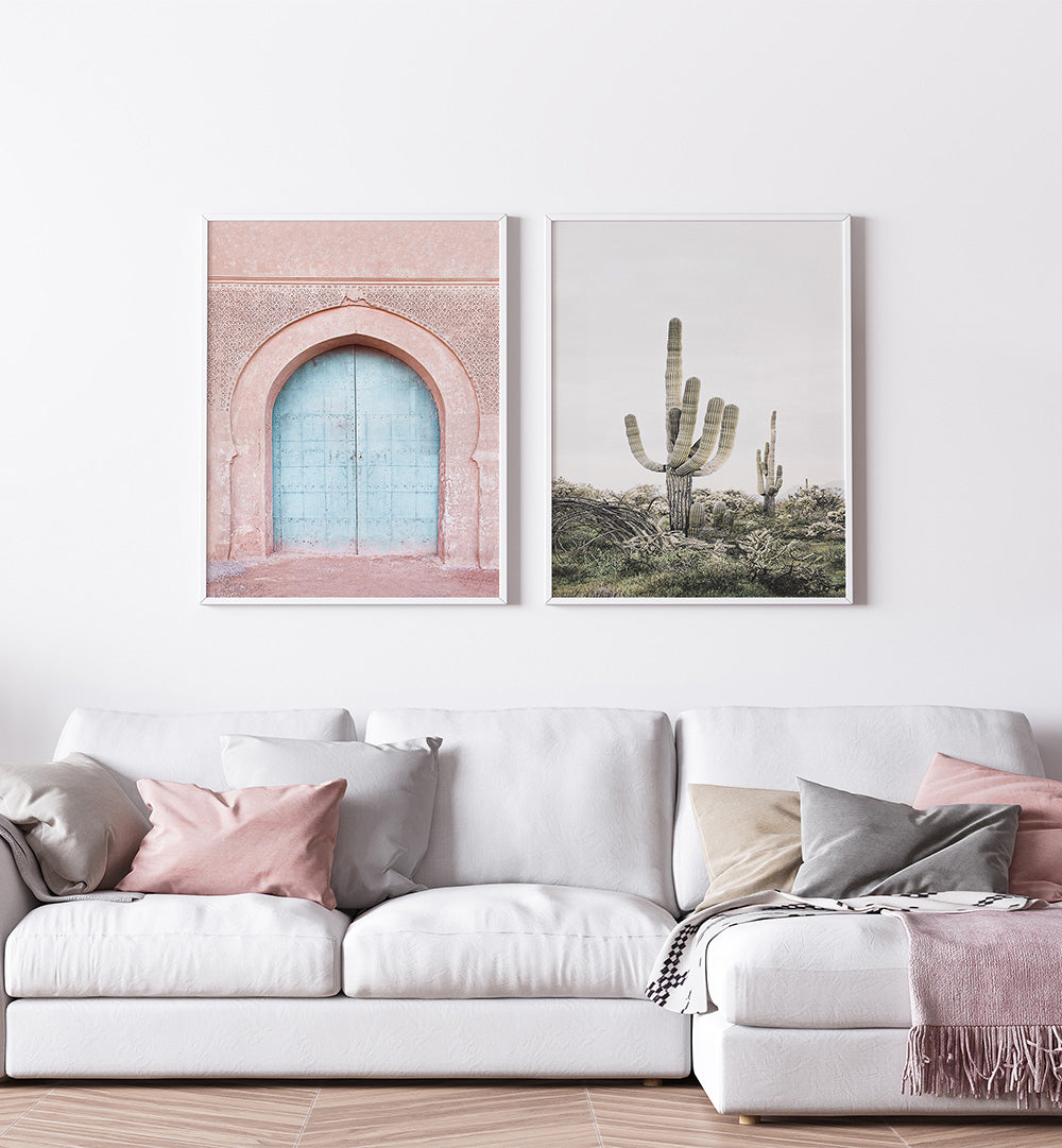 Two framed artworks on a wall above a white sofa with pink and gray pillows.