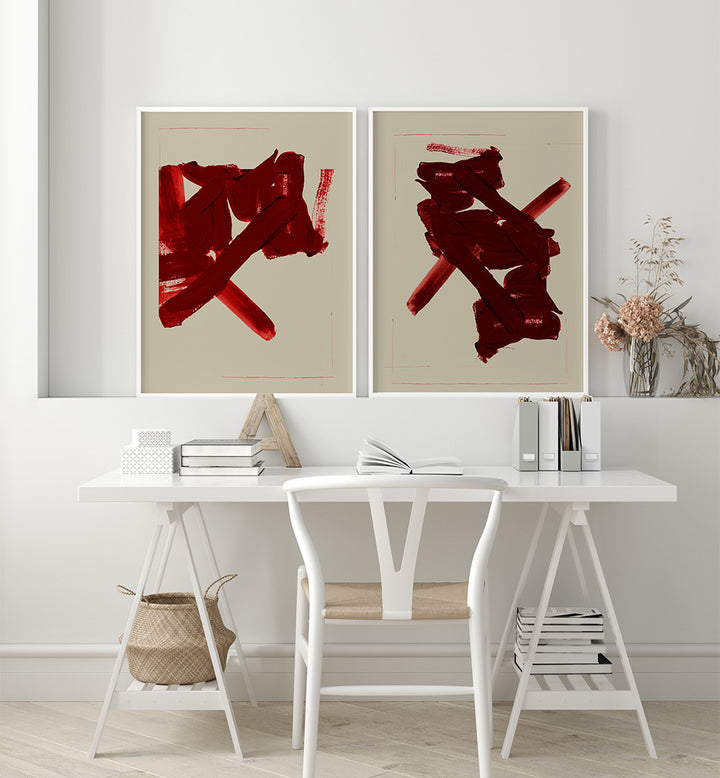 Two abstract red artworks on a wall above a white desk with books and a chair.