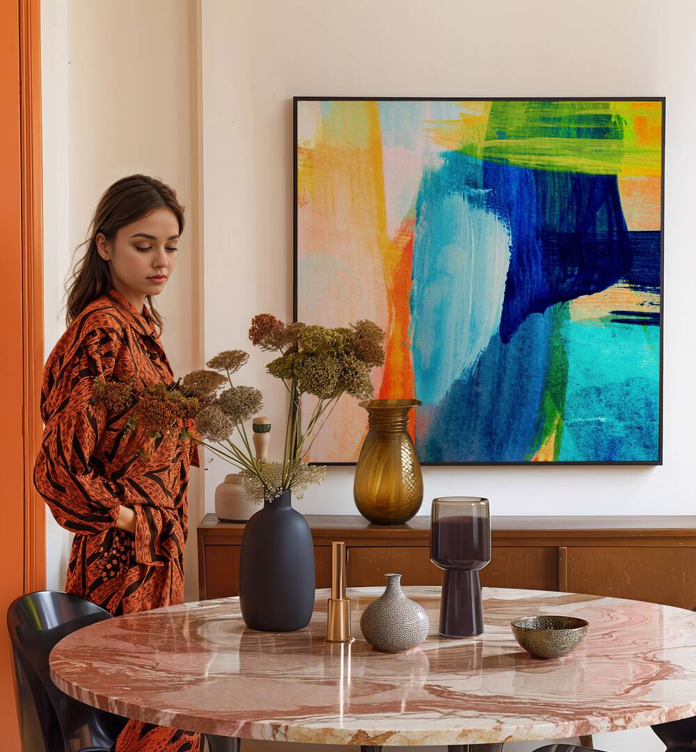 Stylish woman by a table, showcasing TROPICAL HEAT I, ABSTRACT PAINTINGS in a vibrant home decor setting.