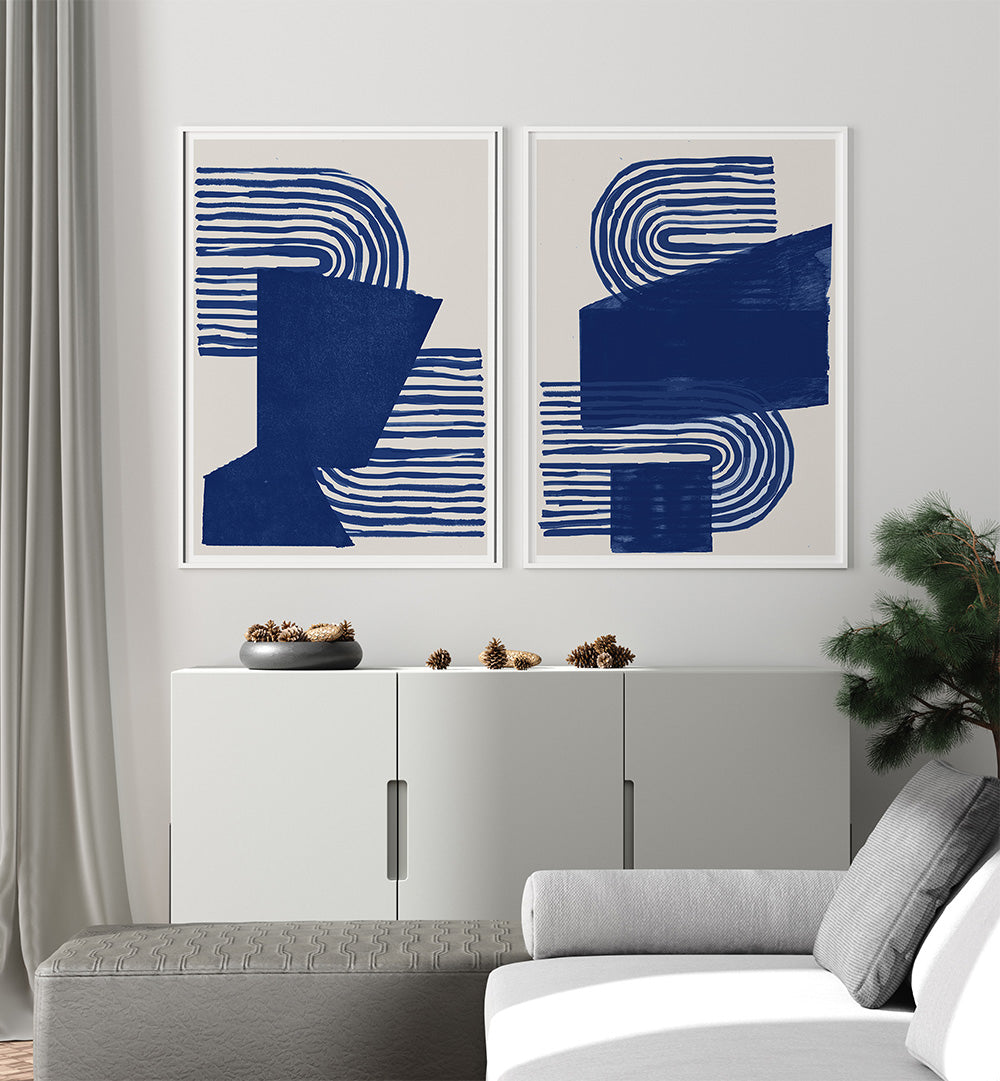 Two abstract blue artworks on a wall above a white cabinet in a living room.