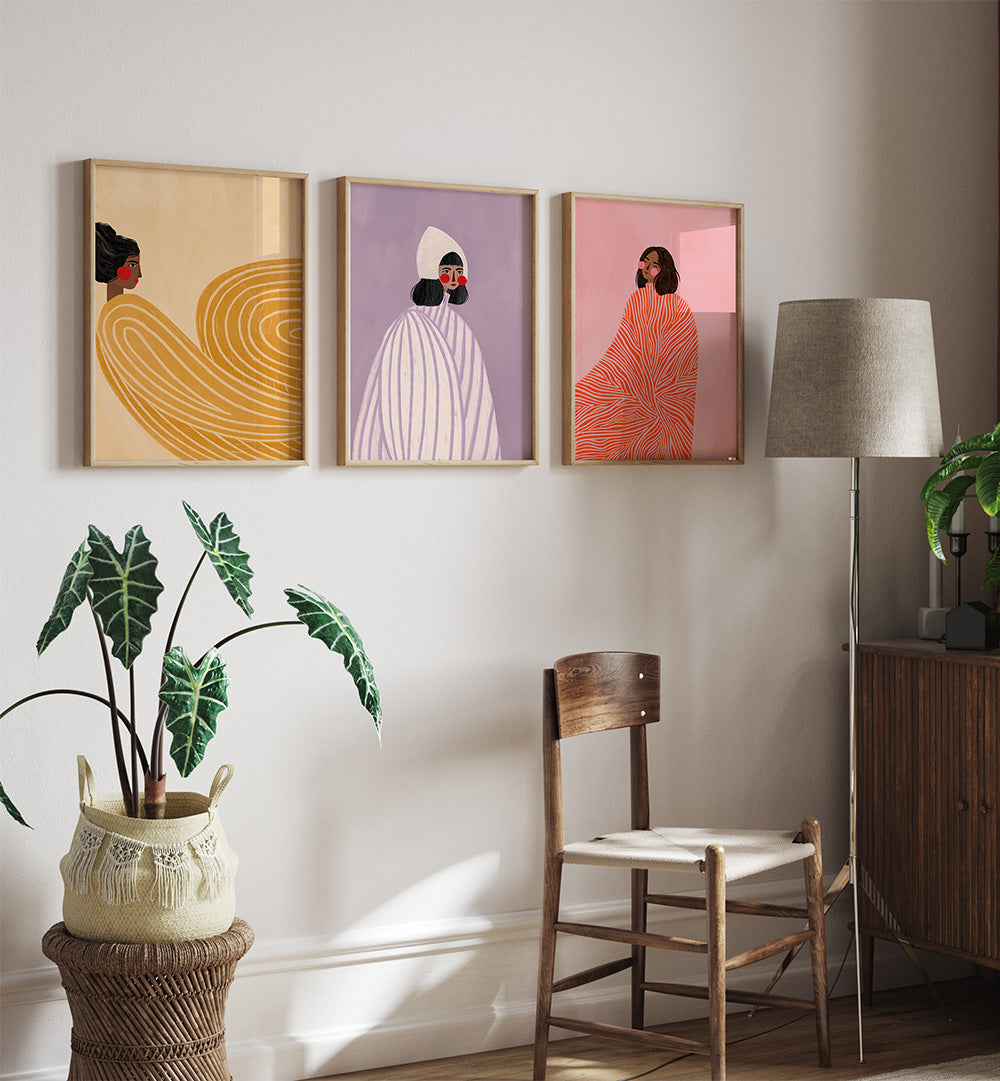 Three colorful wall art pieces on a wall with a chair, lamp, and plant in the foreground.