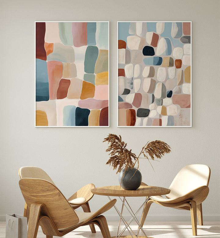 Two abstract wall art pieces above a round table with chairs in a room setting.