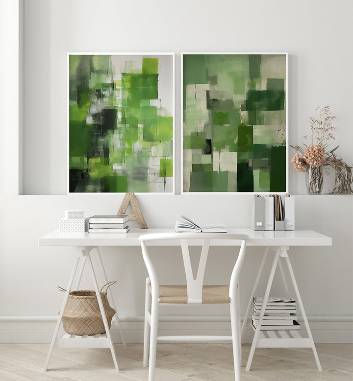 Two abstract green artworks on a white wall above a desk with books and a chair.