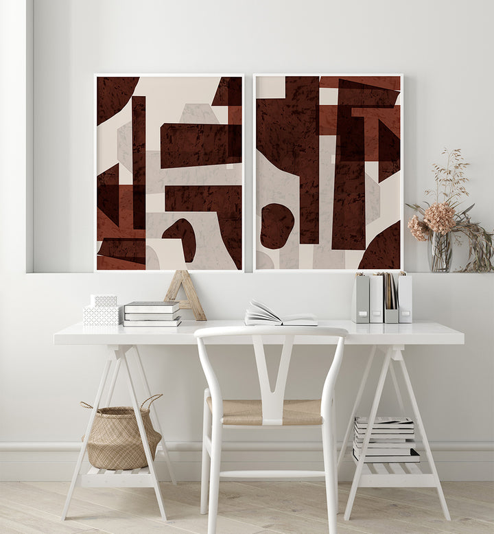 Abstract art pieces on a wall above a white desk with books and a chair.