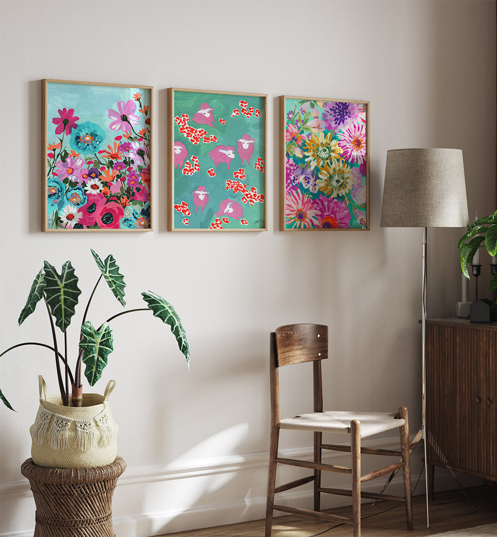 Three colorful floral paintings on a wall above a wooden chair and plant.