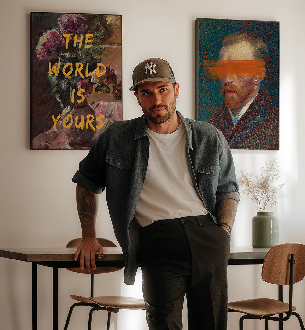 Man standing in a room with two paintings on the wall, one of which says 'The World is Yours'.