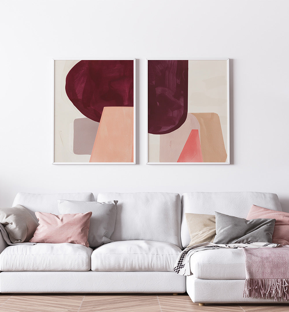 Two abstract art pieces on a wall above a sofa with cushions.