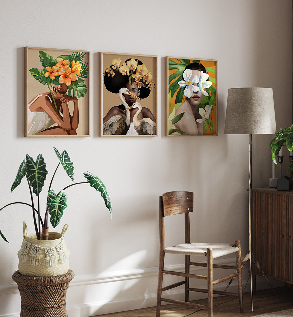 Three framed artworks of women with flowers in their hair in a room with a plant, chair, and lamp.