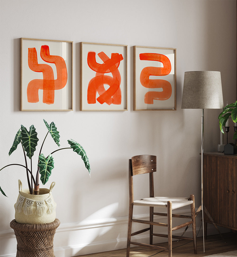 Three abstract orange artworks on a wall with a chair, lamp, and plant in a room.