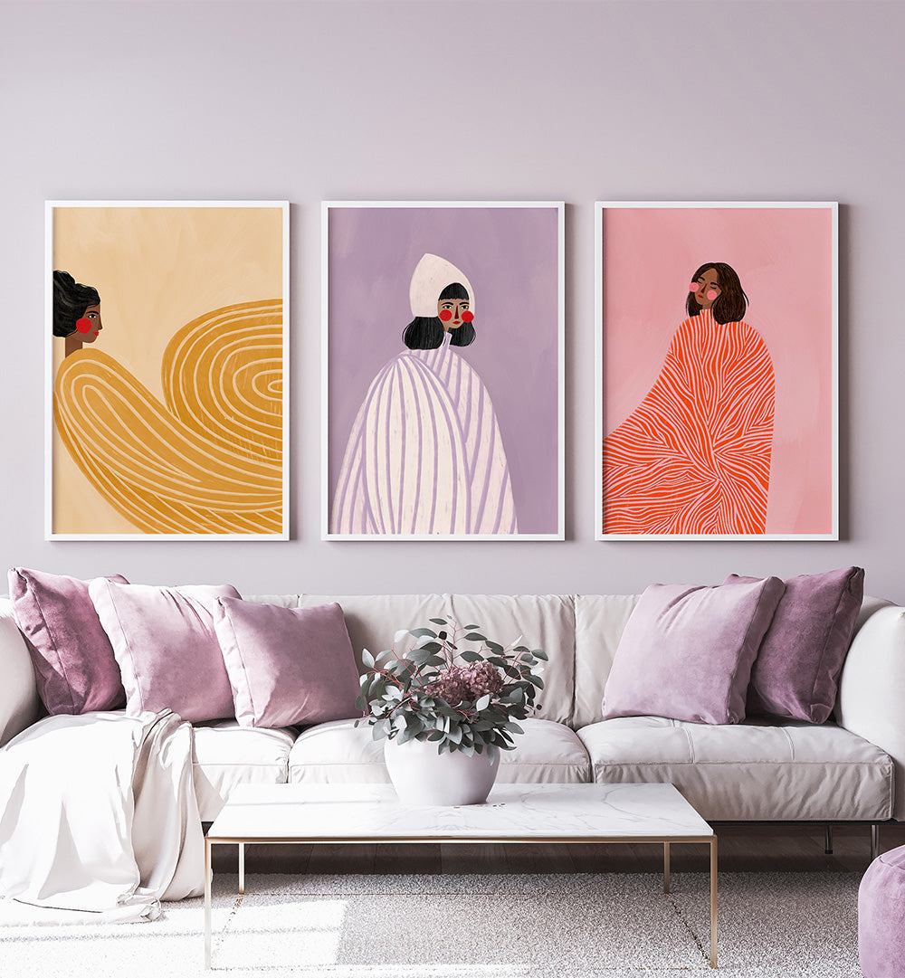 Three abstract art prints on a wall above a sofa with pink and purple cushions.