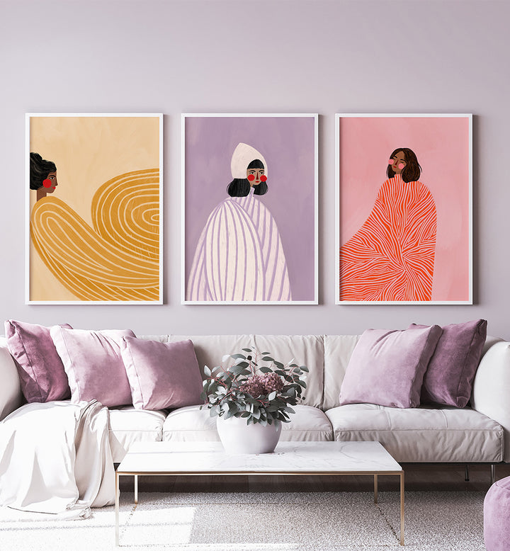 Three abstract art prints on a wall above a sofa with pink and purple cushions.