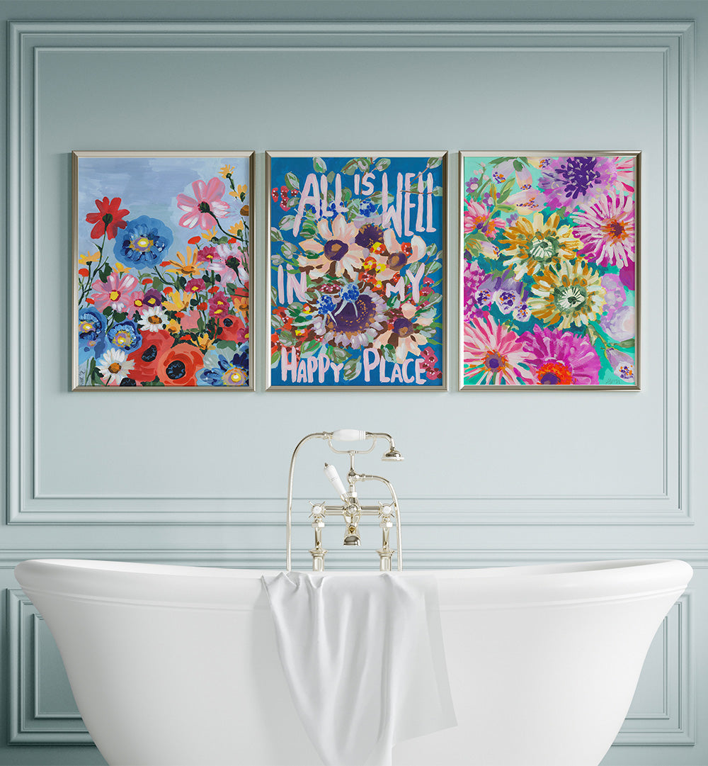 Three colorful floral artworks above a white bathtub with a decorative wall.