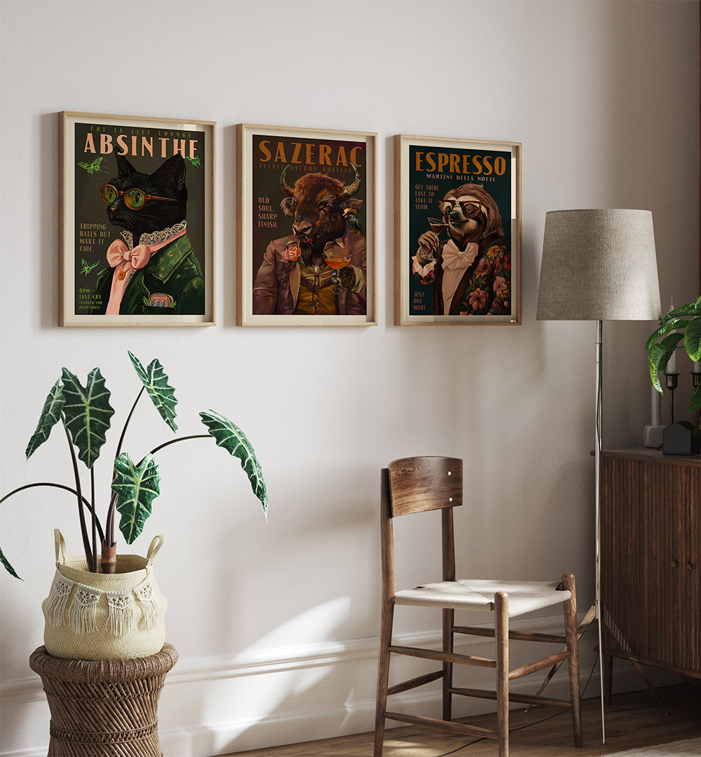 Three framed posters on a wall above a wooden chair with a plant and lamp in the foreground.