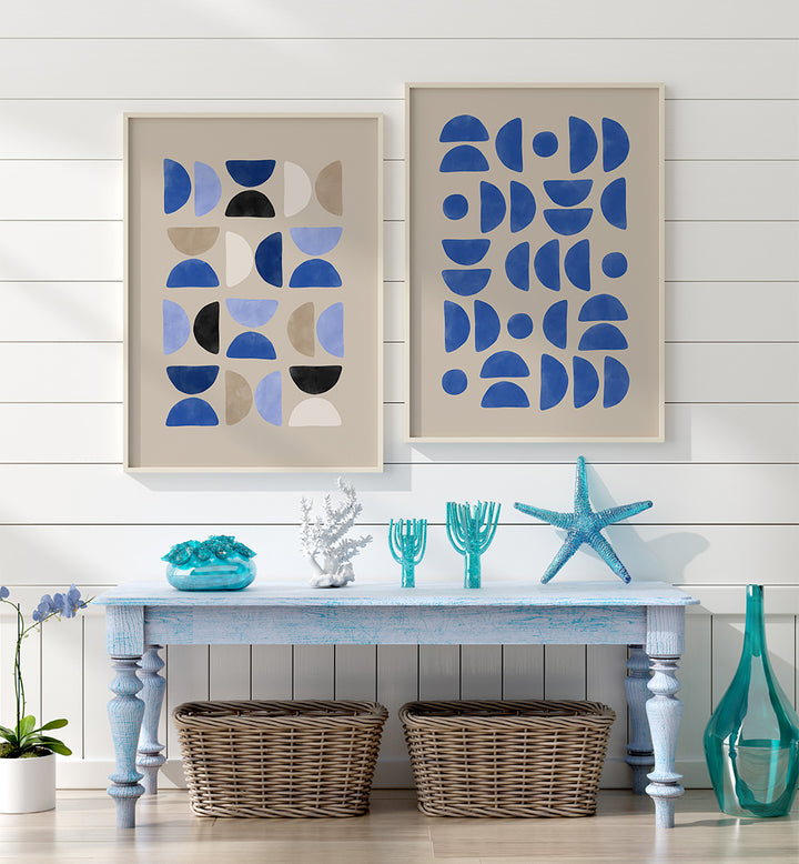 Two abstract art pieces on a wall above a table with decorative items.