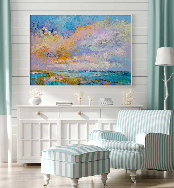 COLORFUL , LANDSCAPE PAINTINGS hung above white console in pastel coastal living room with striped armchair
