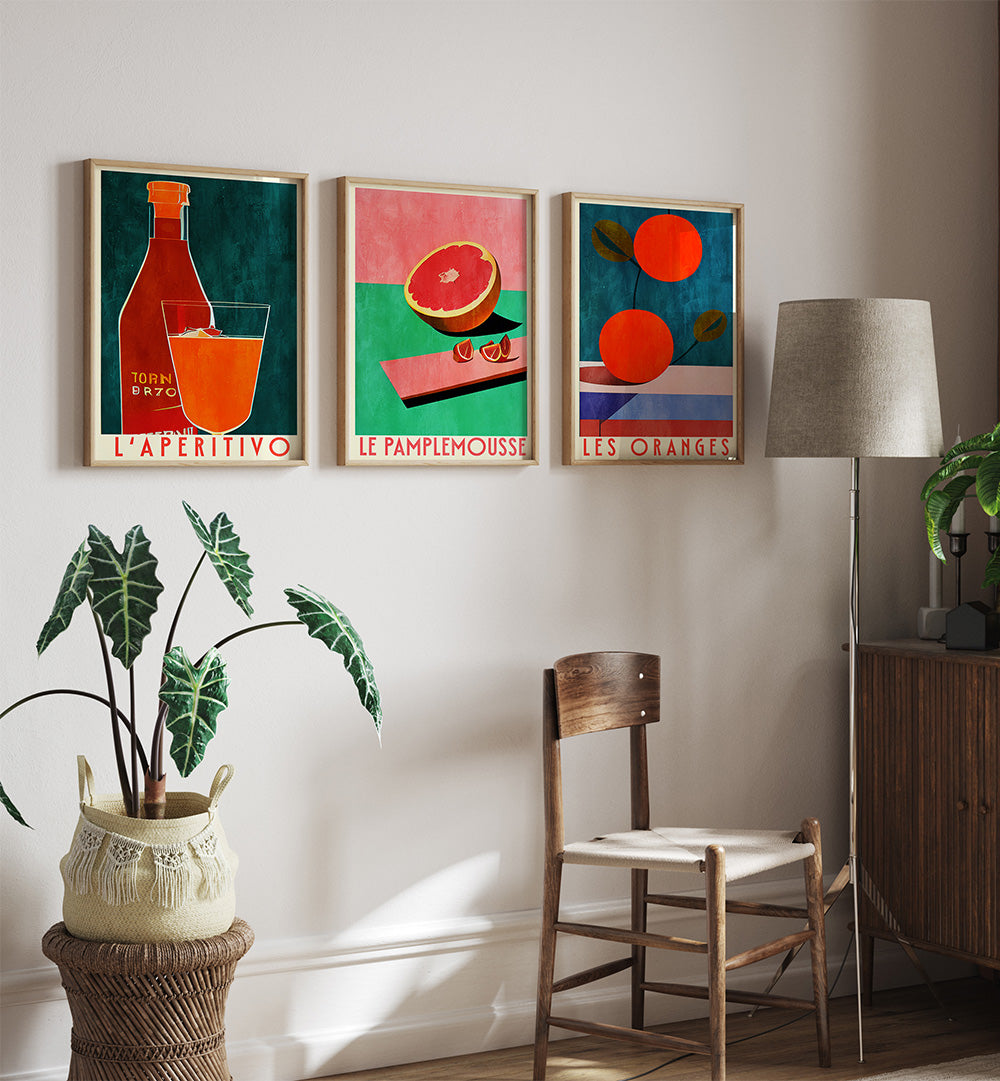 Three colorful framed artworks on a wall with a chair, lamp, and plant in the foreground.