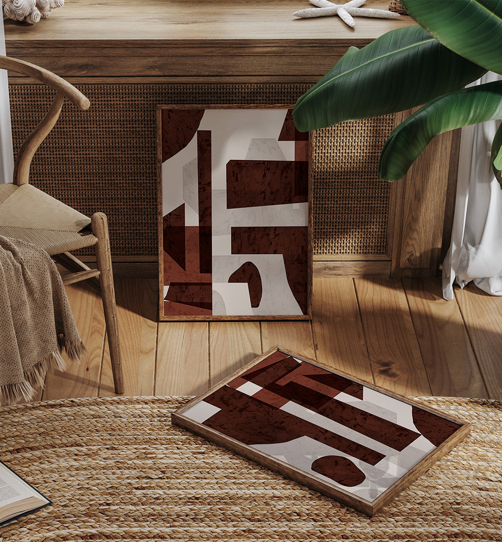 Two abstract art pieces on a wooden floor with a chair and plant in the background.