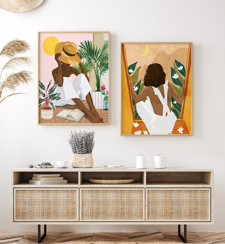 Two framed artworks of women in a tropical setting above a wooden console table.