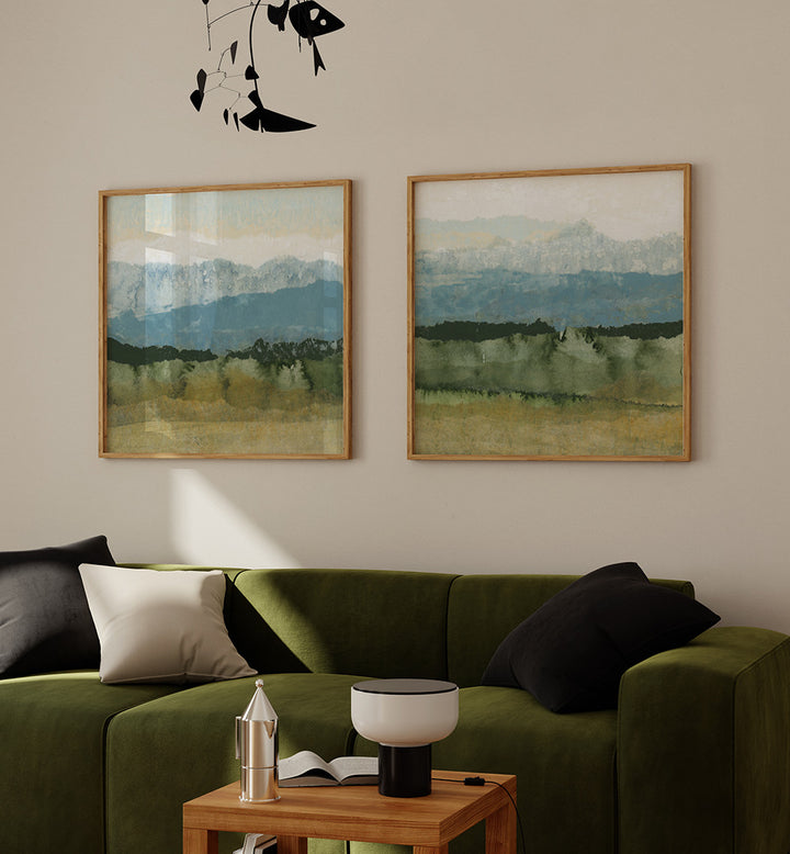 Two framed landscape paintings above a green sofa with decorative pillows.