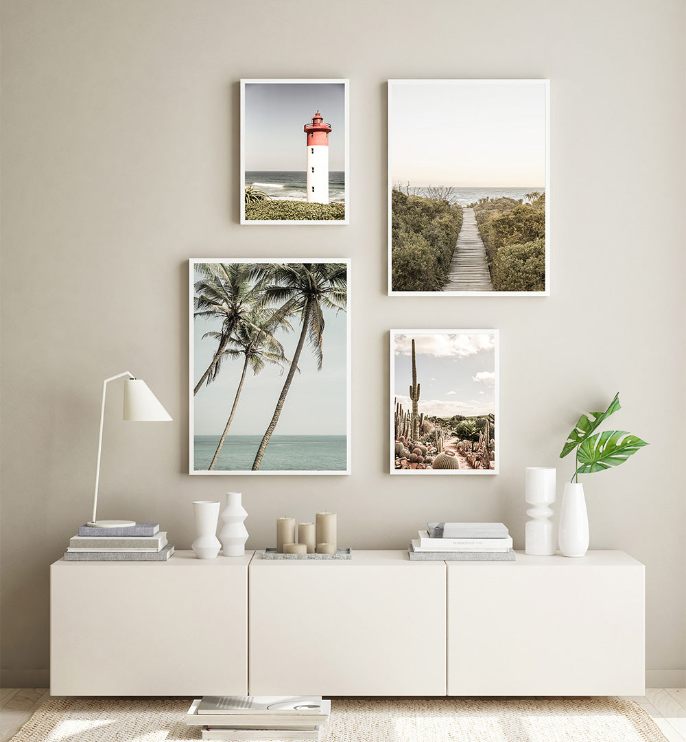 Wall art prints of a lighthouse, palm trees, and desert landscape above a white console table.