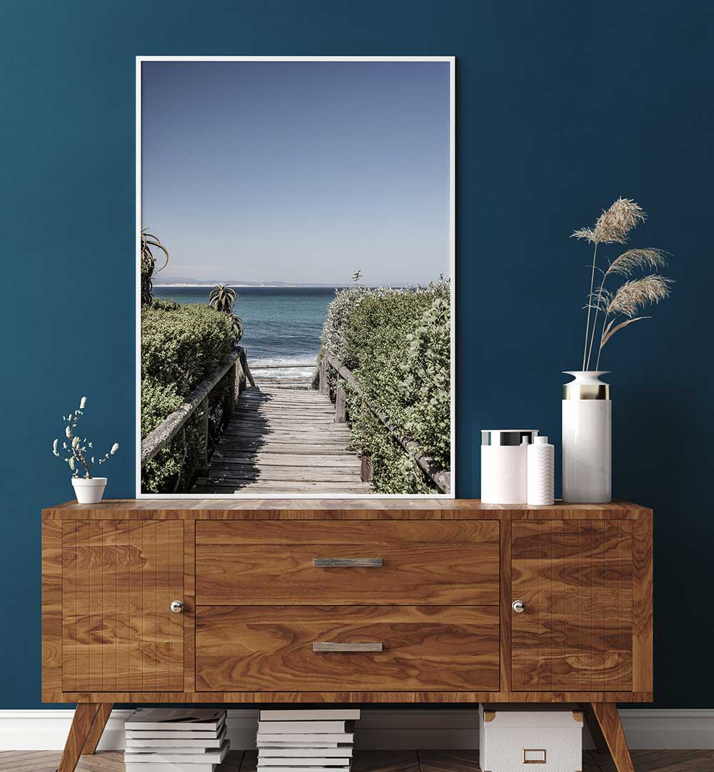 SEASIDE TRANQUILITY , BEACH PAINTINGS framed coastal boardwalk print above wooden sideboard, calm blue ocean horizon