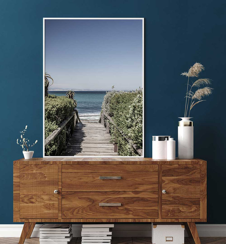SEASIDE TRANQUILITY , BEACH PAINTINGS framed coastal boardwalk print above wooden sideboard, calm blue ocean horizon