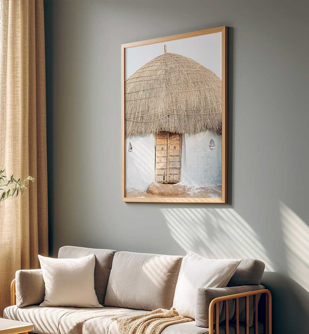 Framed THATCHED HAVEN , INDIAN ART PAINTINGS depicting a rustic thatched hut hanging above a neutral sofa