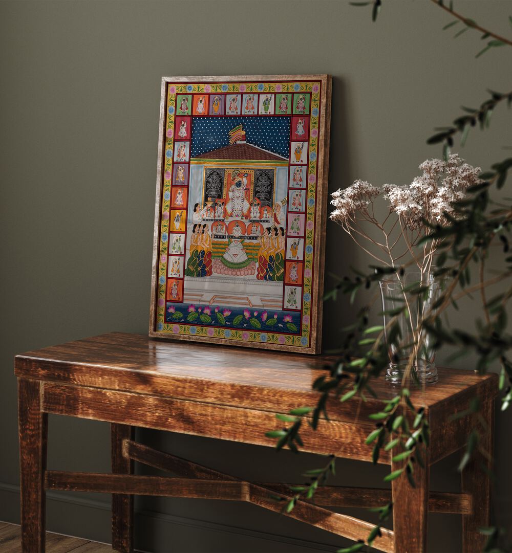 Annakut Pichwai Artwork Indian Art Painting Artwork in oakwood plain frame above a brown table next to flower vase