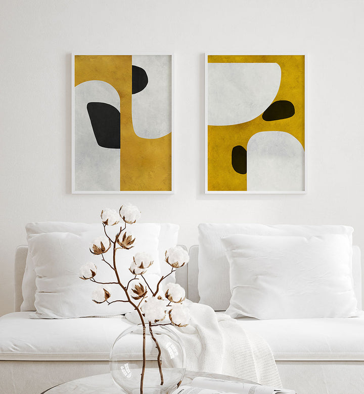 Two abstract art pieces on a white wall above a white sofa with decorative elements.