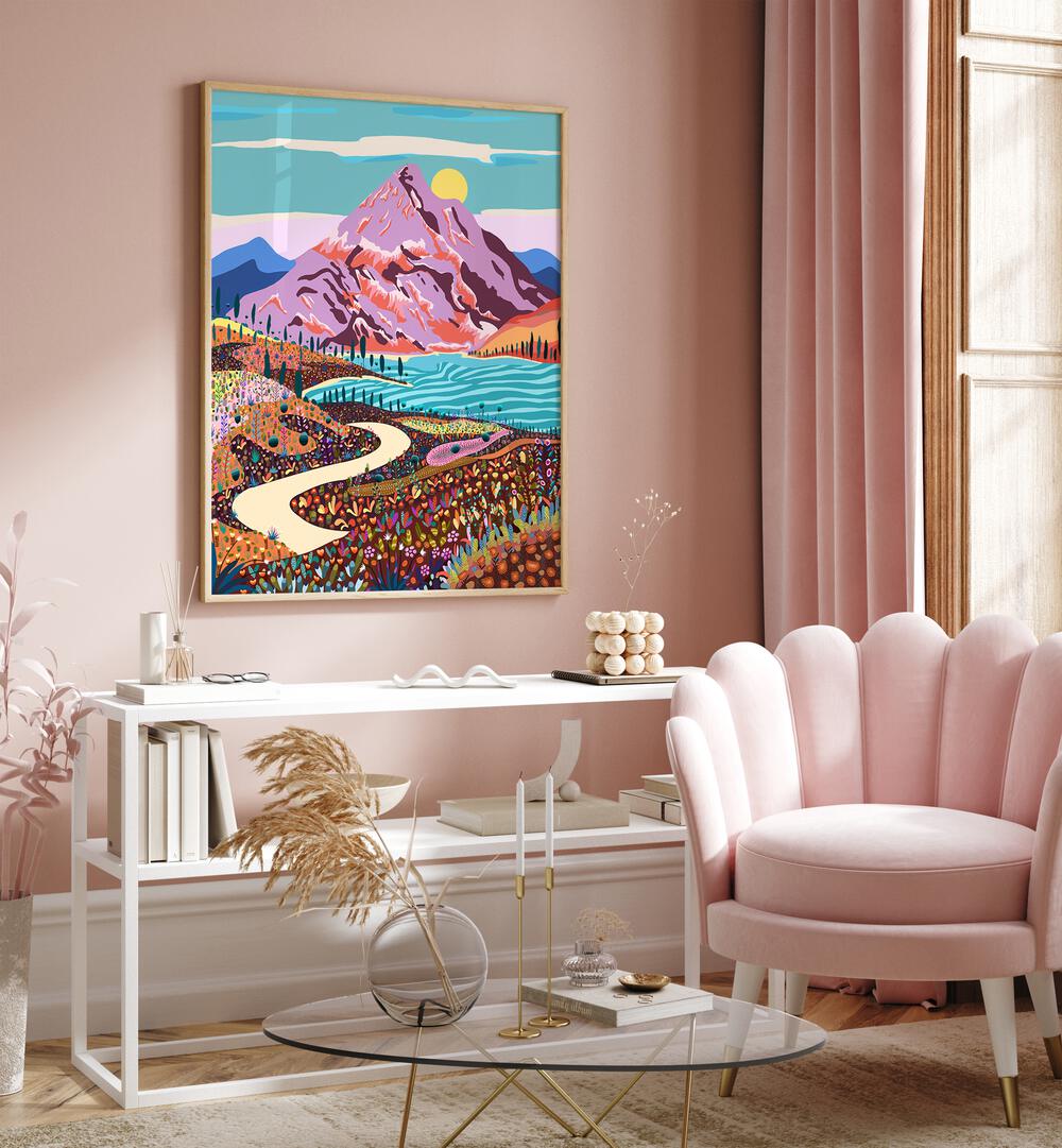 Alice In Wonder Valley By Uma Gokhale Landscape Art Prints in Oak Wood Plain Frame on a pink wall above a white table