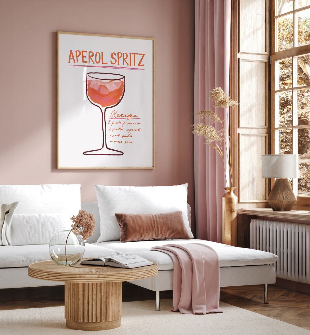 Aperol Spiritz by Athene Fritsch Cafe Art Prints Cafe Posters in Oak Wood Plain Frame placed on a pink wall beside a window and behind a sofa for living room