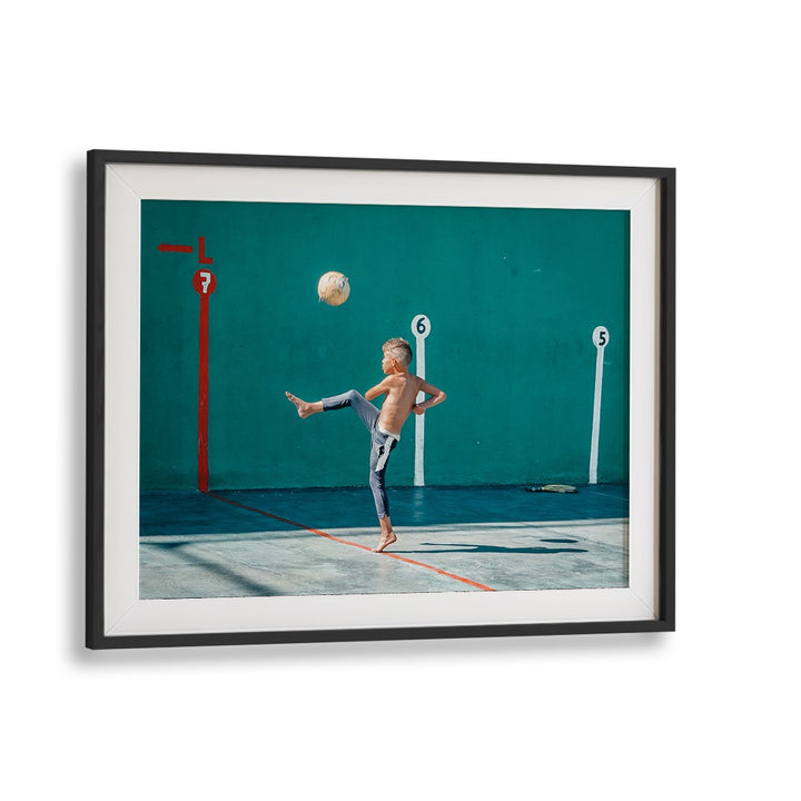 Boy kicking a yellow ball in a vibrant urban setting, perfect for YELLOW BALL, PHOTOGRAPHY PRINTS by Blackmount.
