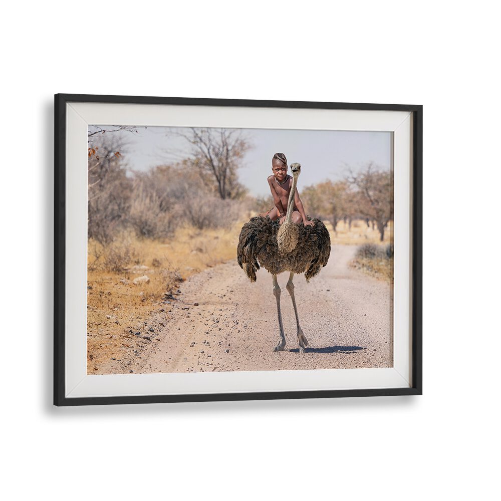 HIMBA RIDE, PHOTOGRAPHY PRINTS showcase a child riding an ostrich on a scenic dirt road, capturing wildlife's beauty.
