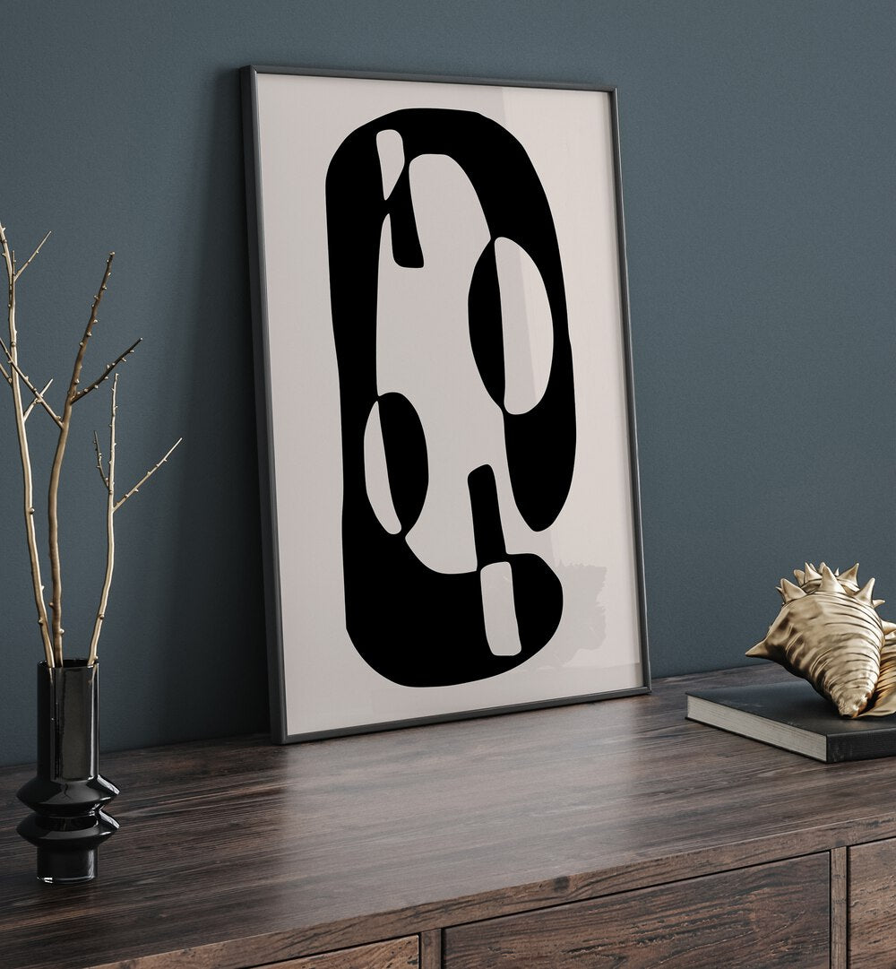 Black And Beige I By Preayna Abstract Art Paintings in Black Plain Frame on a console table beside a flower pot