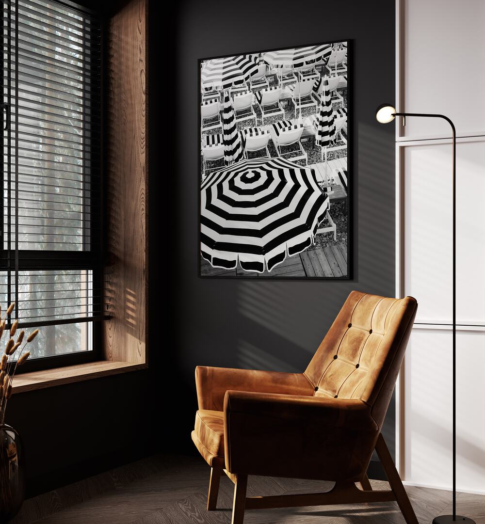 Black and White Beach Umbrellas I By Grace Digital Art Co Beach Prints in Black Plain Frame placed on a wall beside an orange sofa